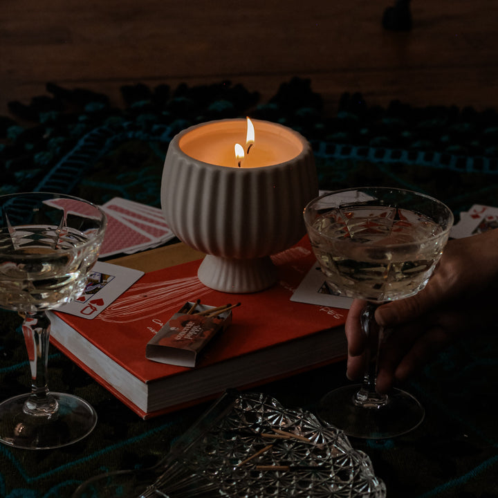 Candlelit scene with glasses, playing cards, and a book on a dark surface.