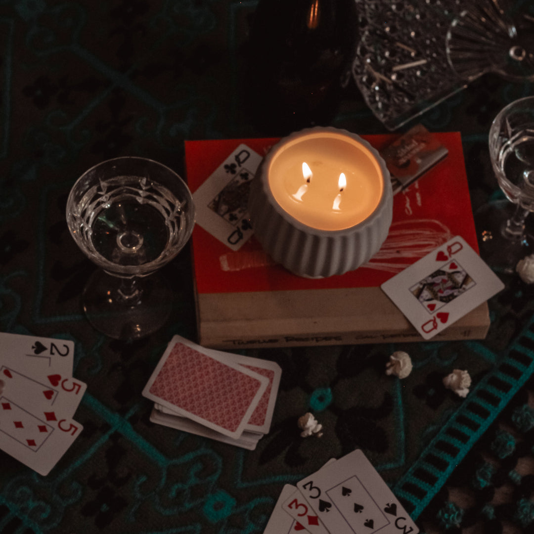 Candlelit scene with playing cards, popcorn, and glasses on a dark surface