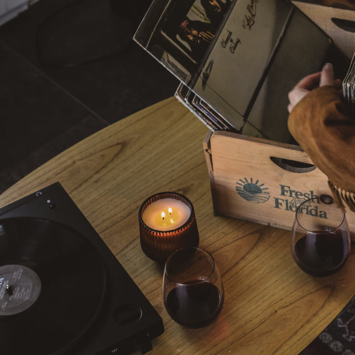 Person opening a record album with a candle and glass of red wine on a wooden table.