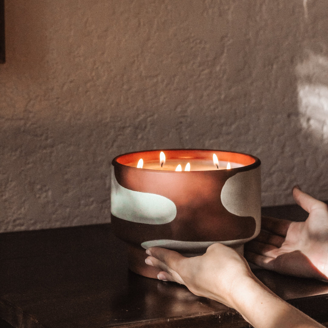 Candle in a decorative bowl being held by a hand against a textured wall.