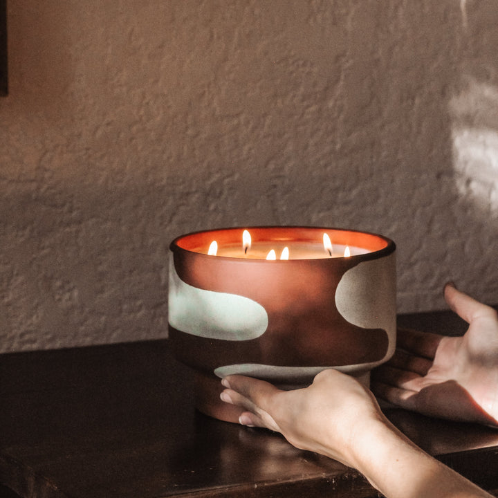 Candle in a decorative bowl being held by a hand against a textured wall.