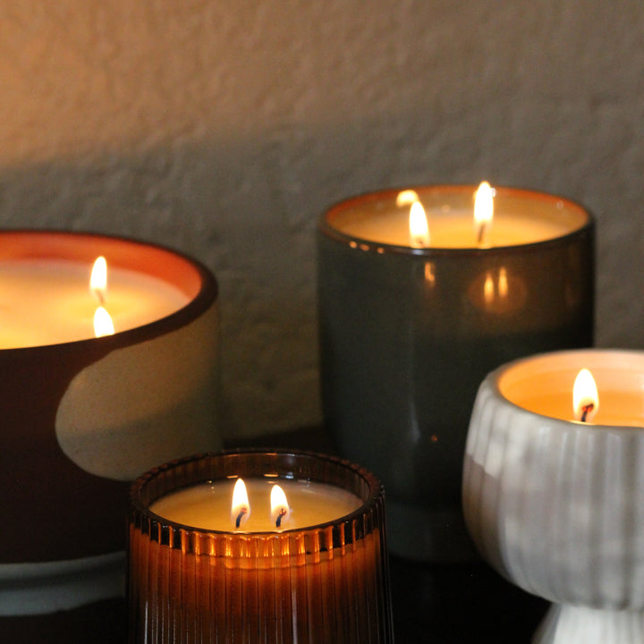 Four lit candles in different holders on a dark surface with a neutral background