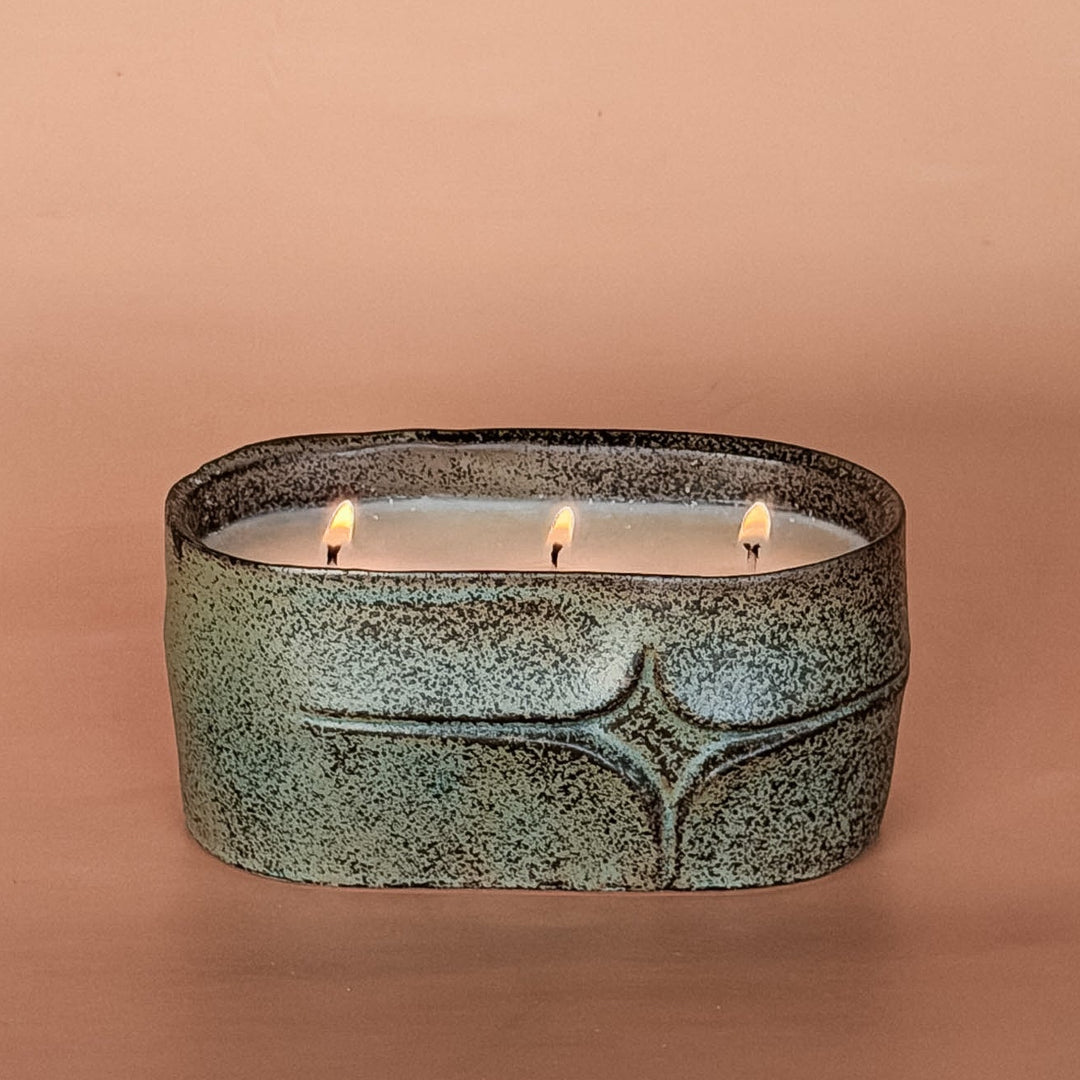 Oval ceramic candle holder with three lit candles on a brown background