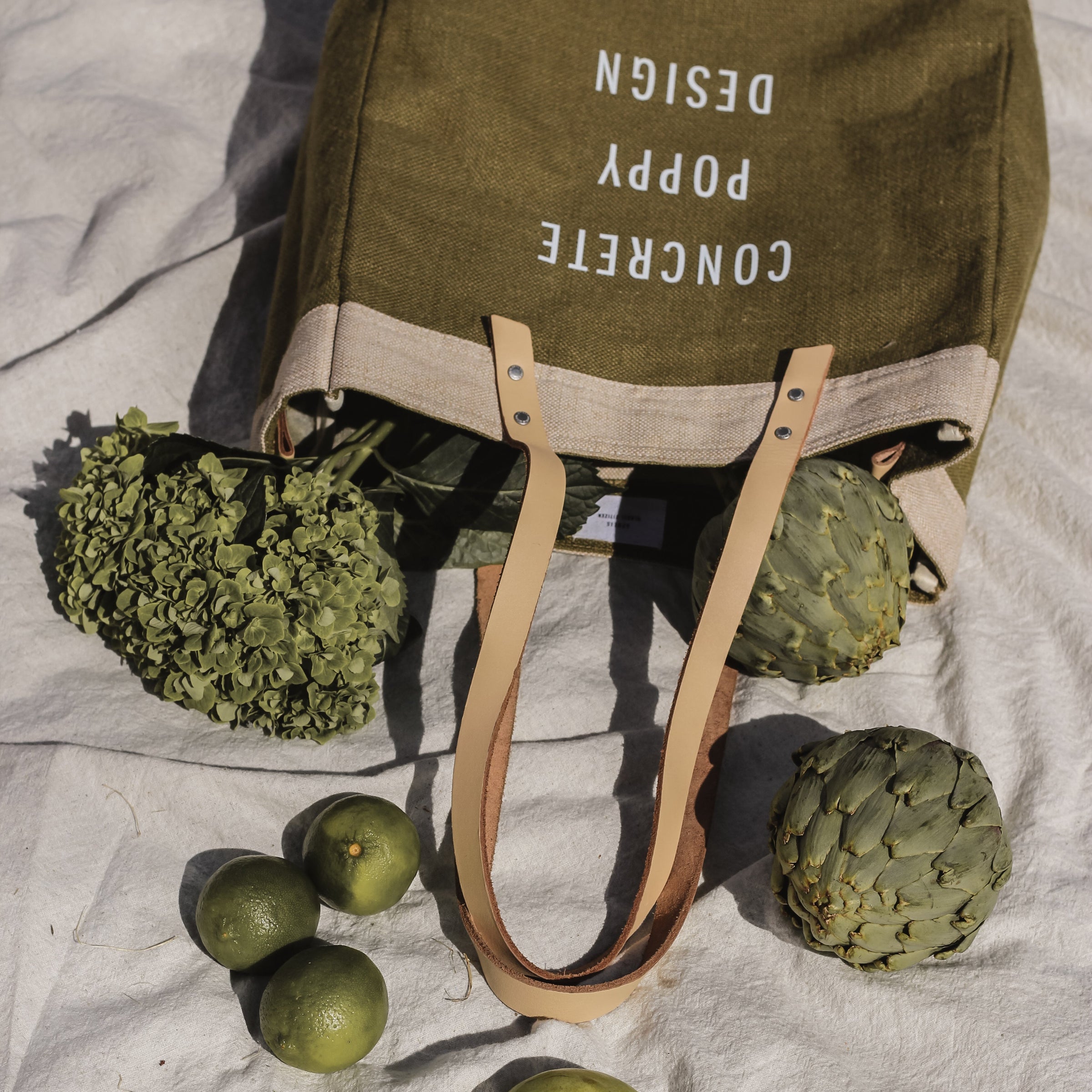 Green tote bag with text, surrounded by green fruits and sunglasses on a light fabric background