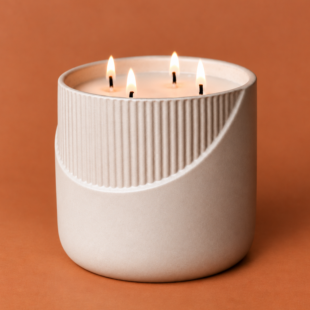 A modern three-wick candle in a ribbed ceramic container with a curved cutout, lit and set against a solid terracotta background.